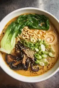 Bol de ramen épicé végan garni de légumes frais et d'herbes.